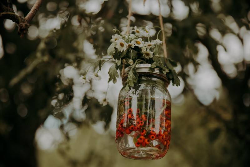 Glass Jar with orange berries and white daisies hanging from tree at wedding ceremony