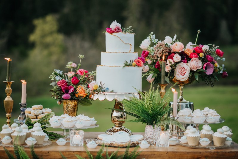 White wedding cake with pink, purple and white roses, peonies and anemones on dessert trolley