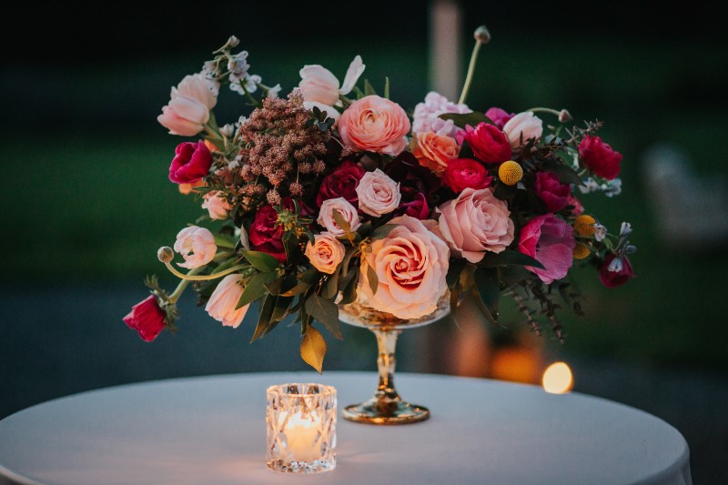 Incredible Wedding Reception Floral Arrangement in gold candlestick with roses anemones, peonies in pinks and purple tones by Lauren Riley