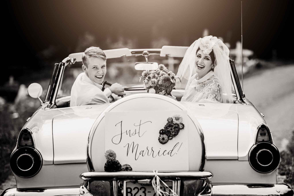 Retro newlyweds wave from vintage car with just married sign 