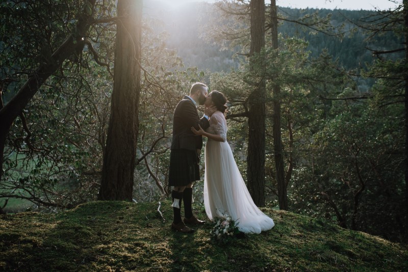 Newlyweds kiss in the forest with sunrise behind them by Three Sisters Photography