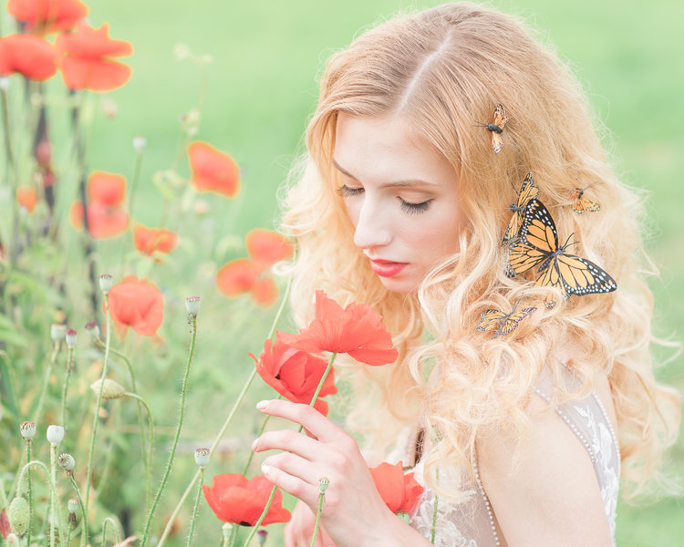 Bride smells orange poppies in LuxxNova wedding gown with butterflies in her hair