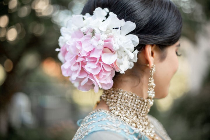 Bride wears pink and white dahlias in her hair along with diamond jewelry