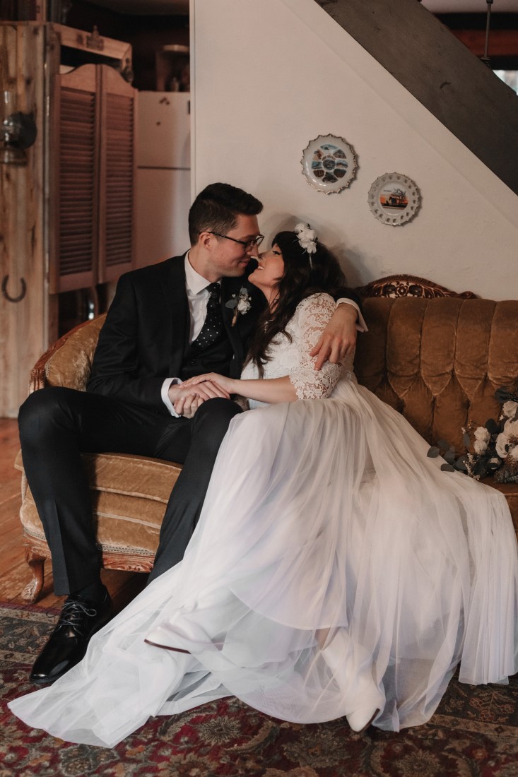 Newlyweds sit on wood bench with brides gown all around them