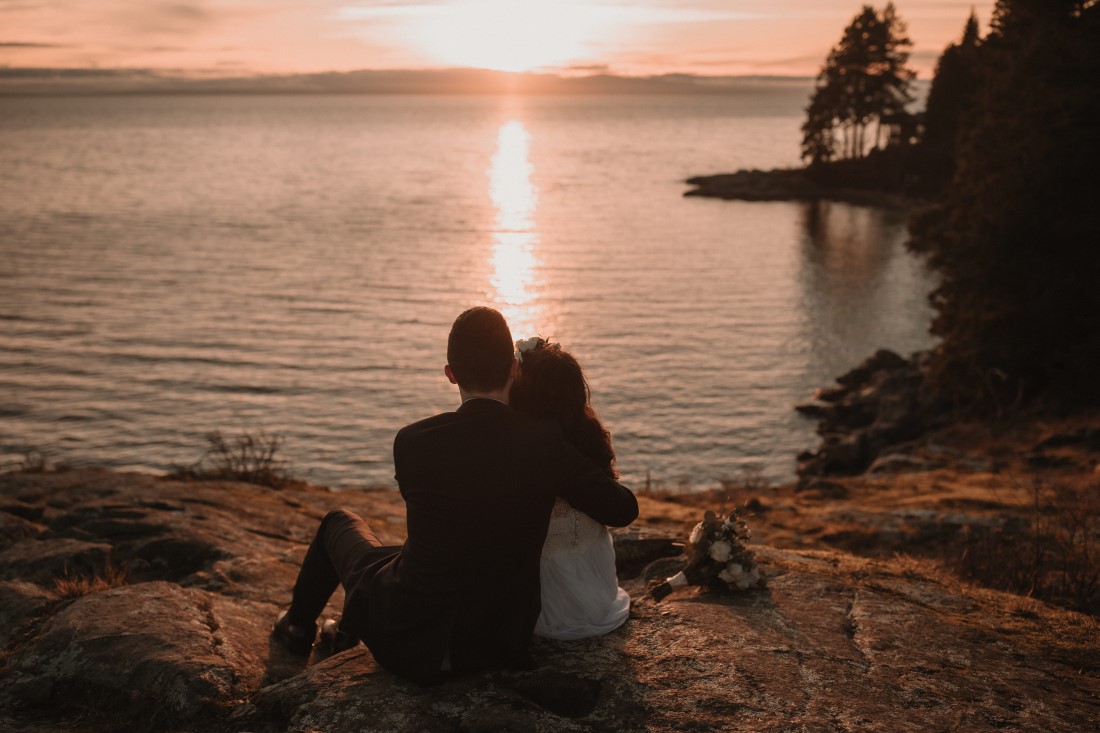 Bride and groom sit on beach and watch the sunset by Jennifer Picard Photography