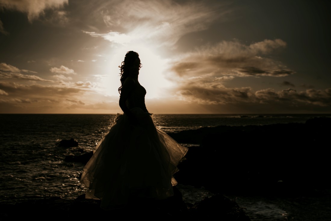 Bride standing beside the ocean is highlighted by the sunset in Tofino Vancouver Island