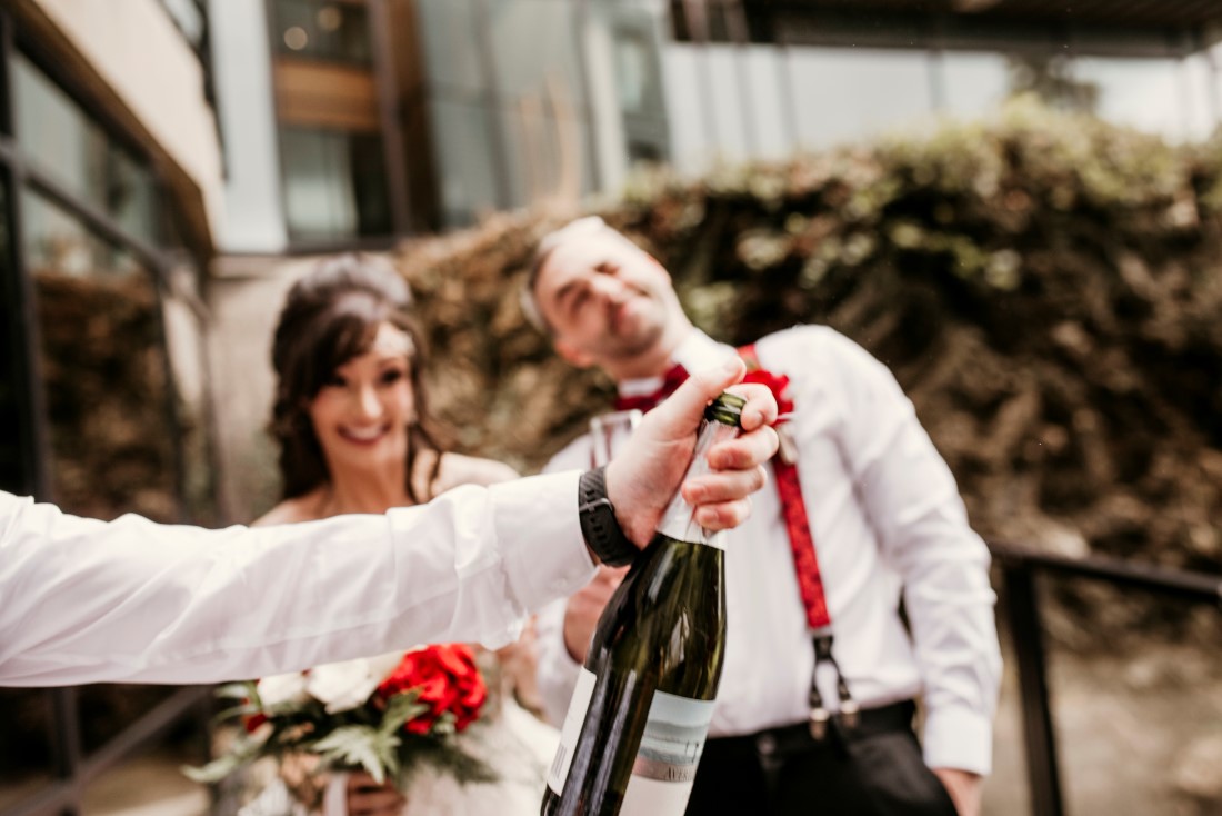 Newlyweds celebrate with champagne while holding rose bouquet by Crabapple Floral Tofino 