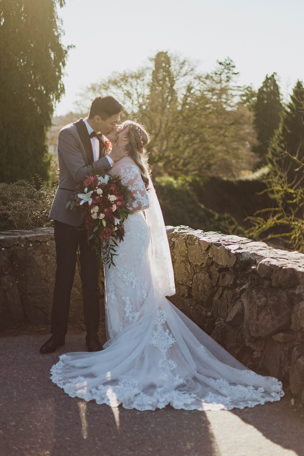 Newlyweds kiss in the sunset with bride wearing lace gown with train and veil by Blush Bridal Victoria 