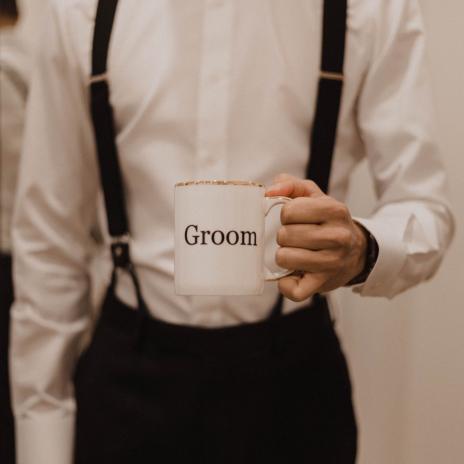 Groom in black suspenders by Surmesur holds groom mug 