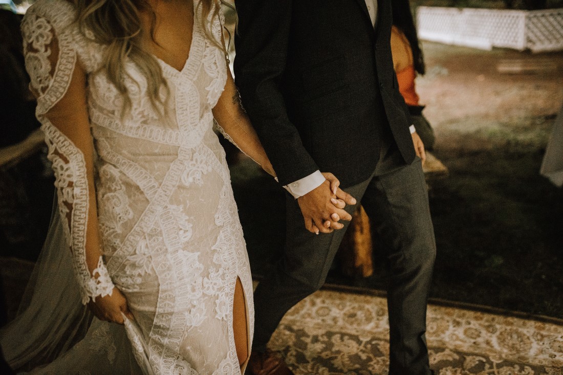 Bride and groom hold hands while walking through field at Farm Table Inn Lake Cowichan 