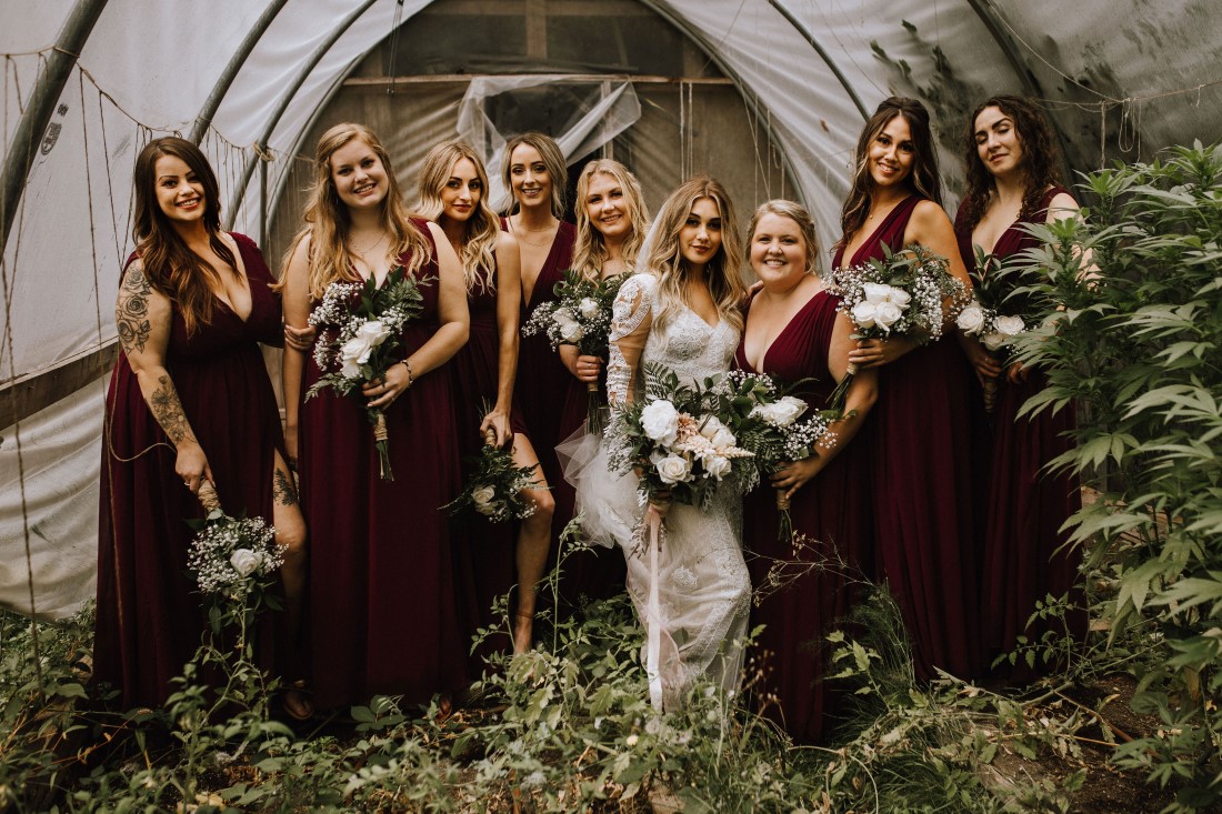 Bride and Bridesmaids in burgundy gowns smile and laugh in a field 