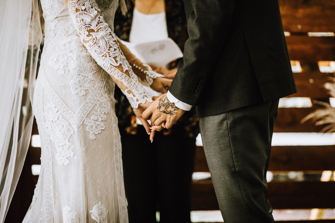 A Farm Table Wedding Couple hold hands during their vows by Flourish Events