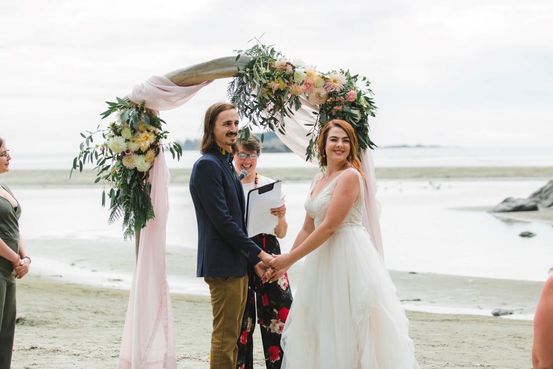 Bride and Groom ceremony in front of arch wrapped in white fabric on Tofino beach