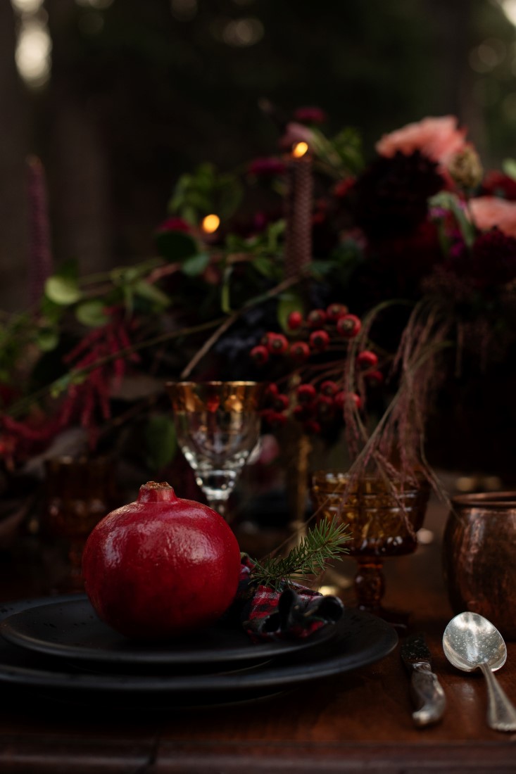 Pomegranate sits on black plates on wedding reception table in the woods