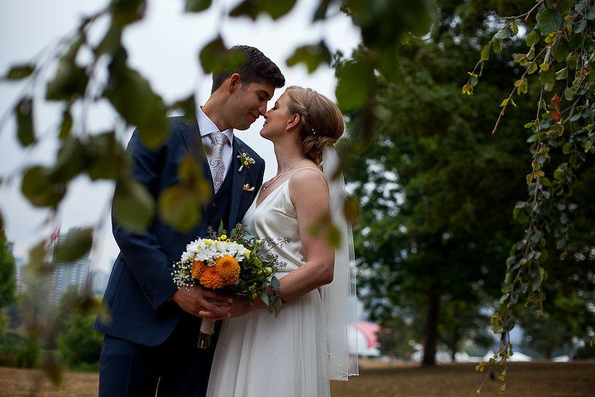 Wedding Couple in the trees of Vancouver holding orange and white gerbera daisy bouquet