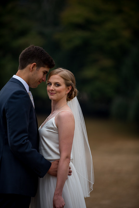 Bride smiles at the camera as groom holds her by Meghan Andrews Photography