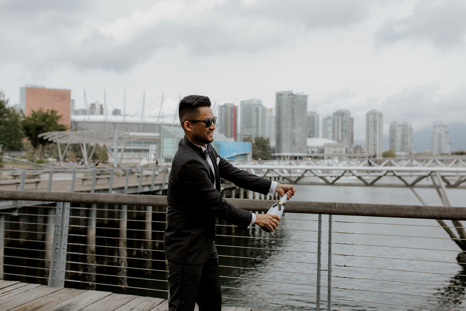 Asian Groom opens champagne bottle on Vancouver water edge 