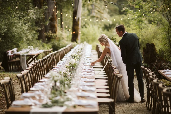 Bride and groom set name cards on long table wedding reception tables in the forest