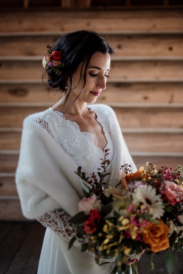 Bride in white stole looks down at bouquet of orange and yellow flowers by Senka Flowers and makeup and hair by Kerry Waring 