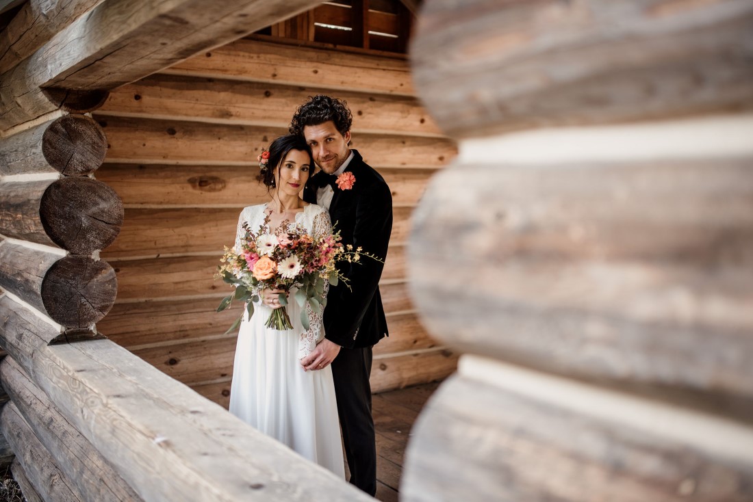 Stone Circle Whistler newlyweds pose by log wall by Emily Serrell