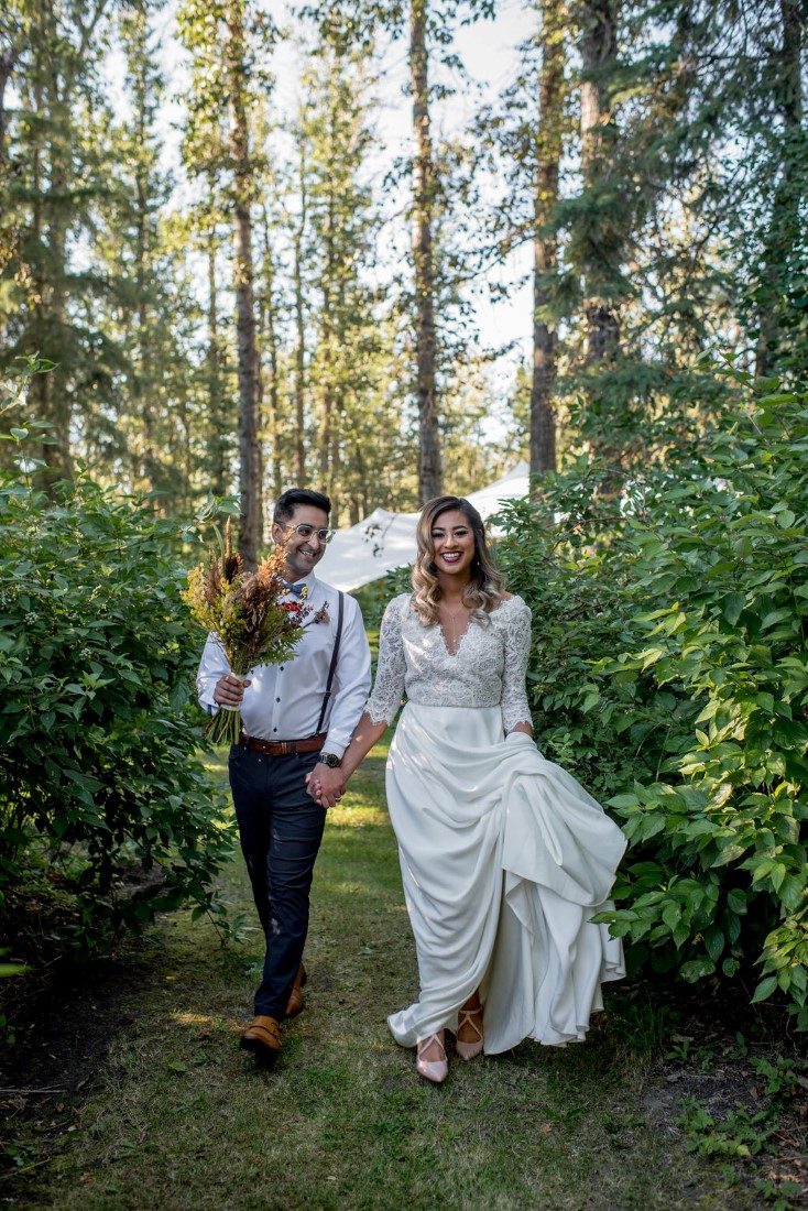 Newlyweds walk through the forest holding hands