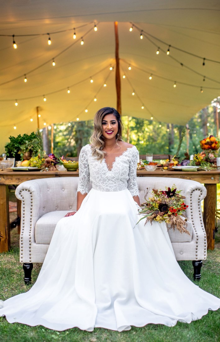 Bride wearing Truvelle gown sitting on settee in field 