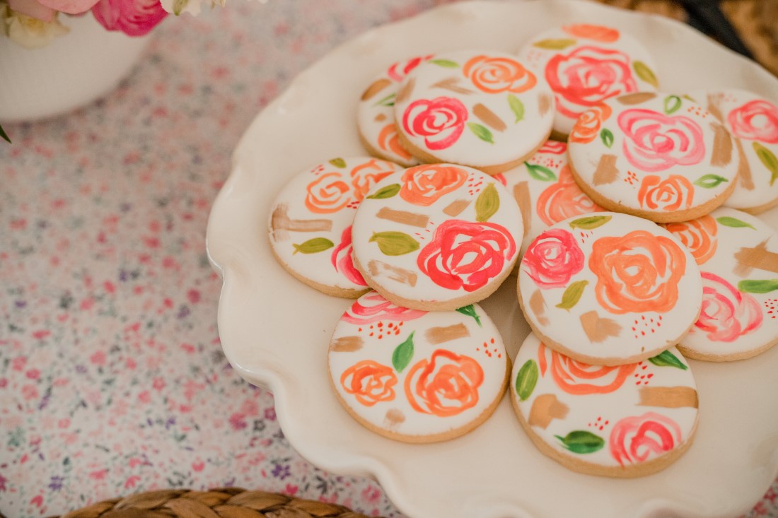 Hand painted cookies with pink flowers on white cake plate by Cake n Sweets Vancouver