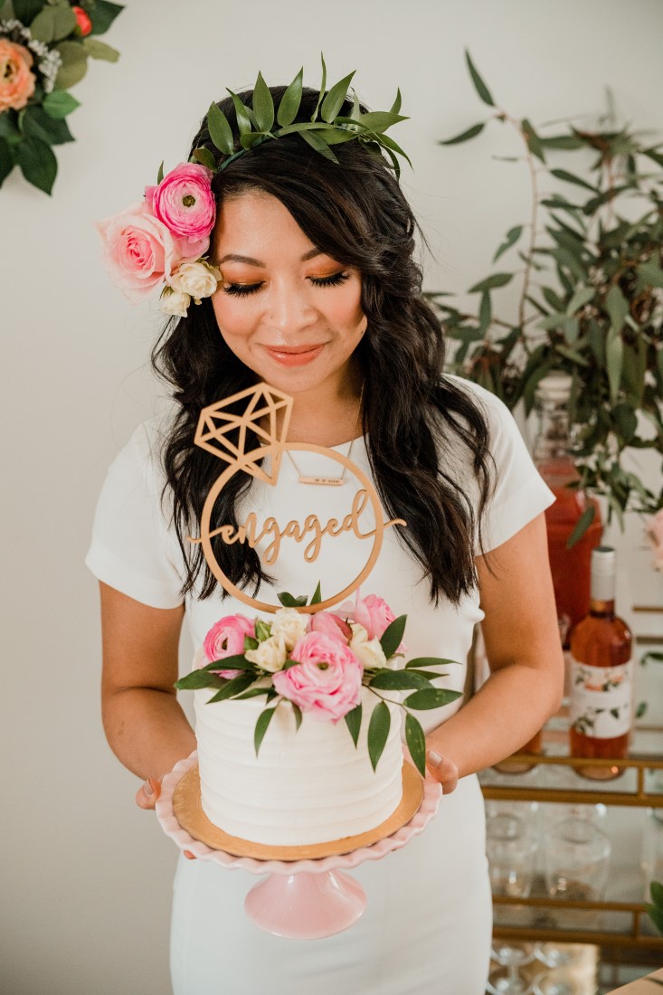 Bride holds shower cake with blush pink flowers and gold topper