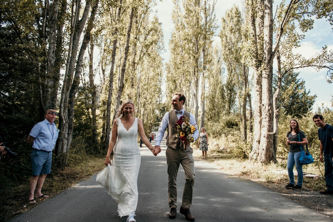 Bride and groom walk towards guests lining sides of road at Covid-19 wedding