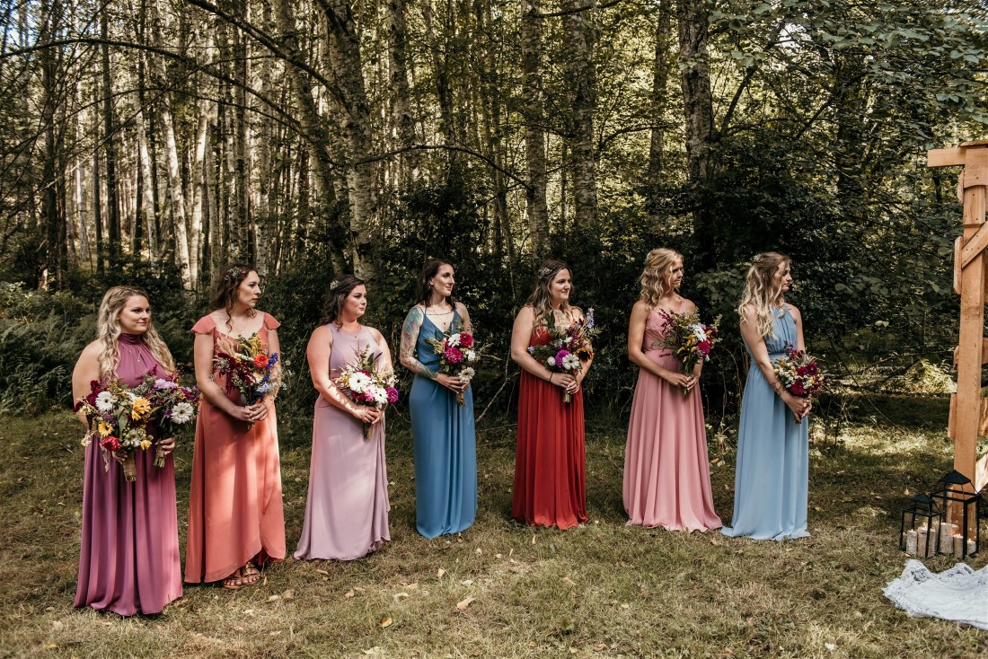 Bridesmaids in multi colored gowns holding wildflowers