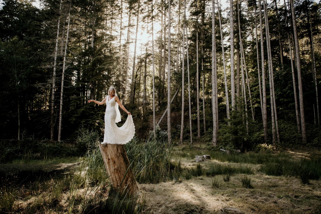 Bride poses on tree stump in BC forest by Coastline Living Photography