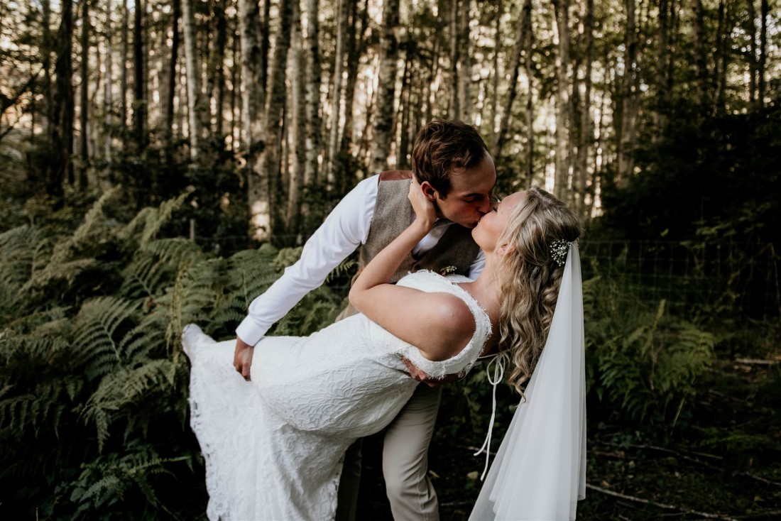 Groom kisses bride in forest on Vancouver Island