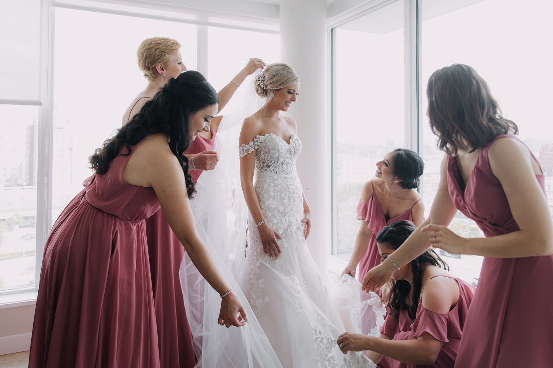 Bridesmaids wearing blush pink gowns help the bride with finishing touches while getting ready in Vancouver