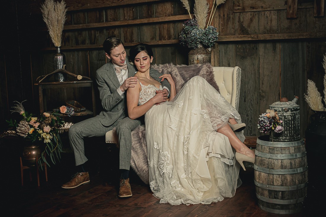 Bride and Groom on settee surrounded by antique wood, barrells, pampas grass and flowers at Langtry Walk