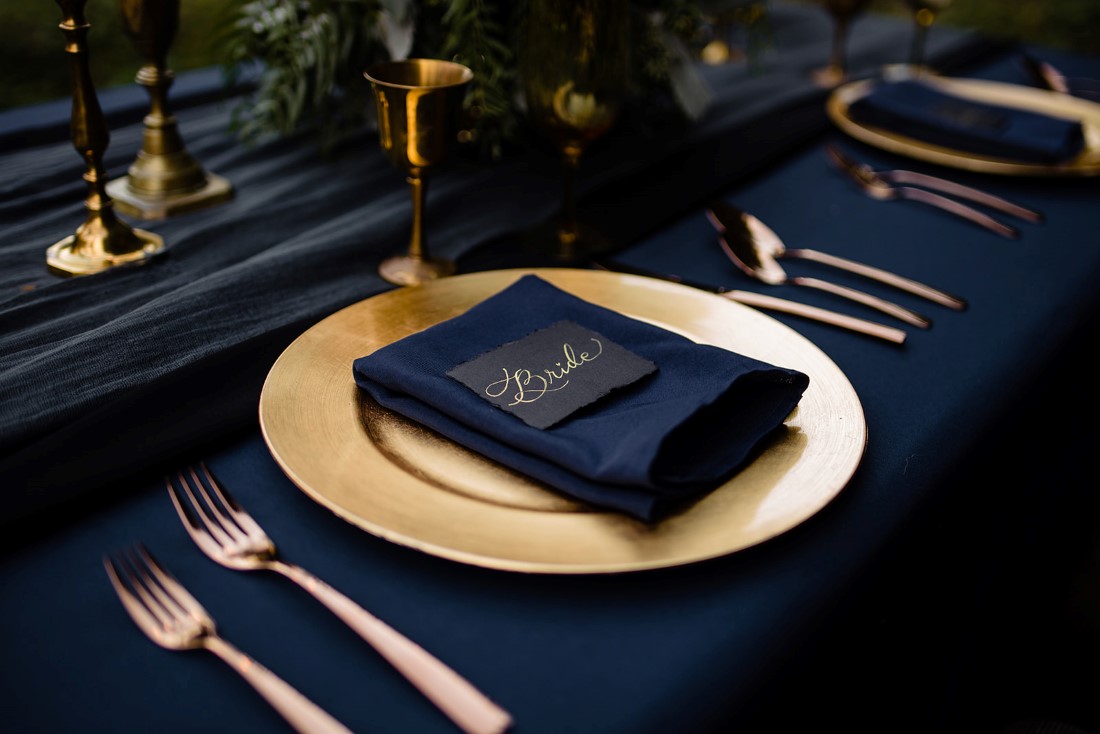 Gold plate and cutlery on black linen with napkin and place card by Pretty Things Rental Vancouver