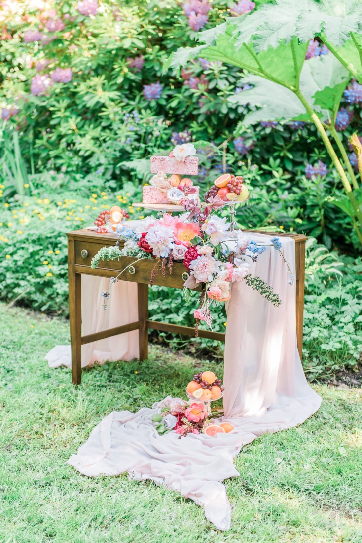 White fabric pools off sweetheart wedding table filled with cakes and flowers in Vancouver park