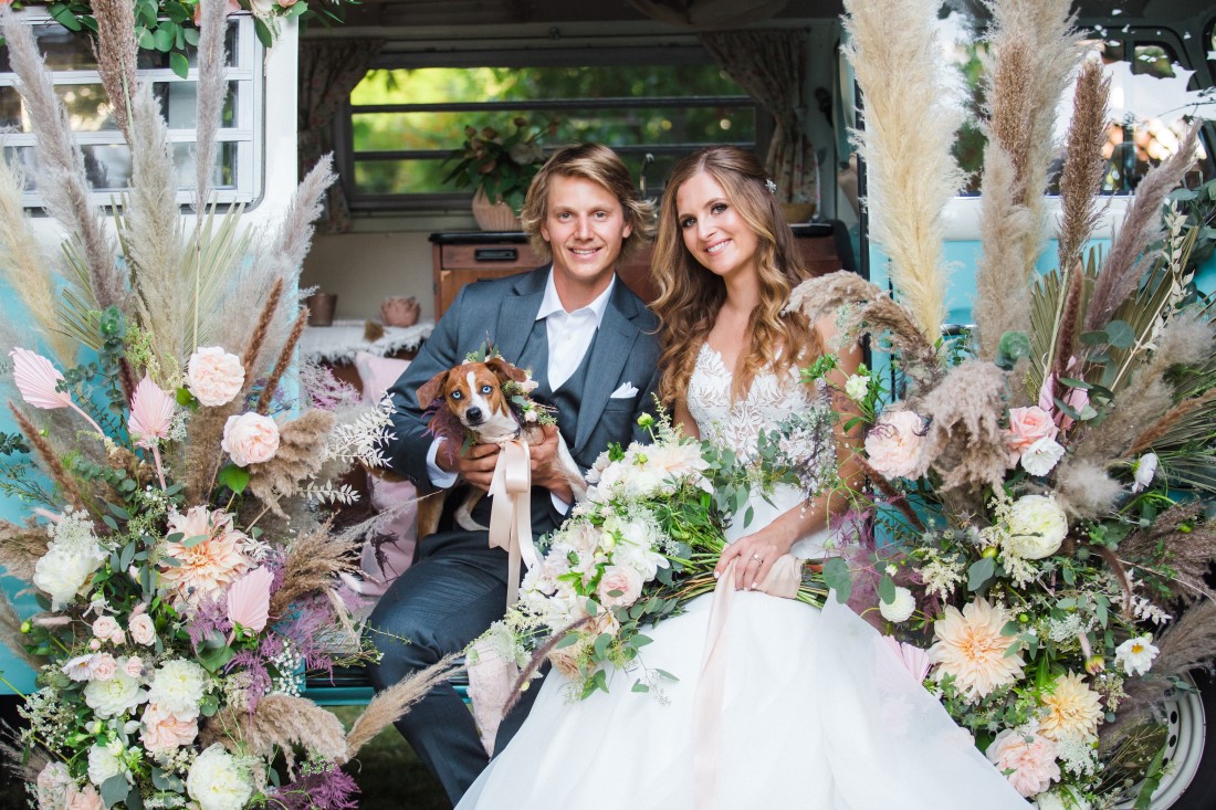 Dog sits on newlyweds who are surrounded by wedding flowers