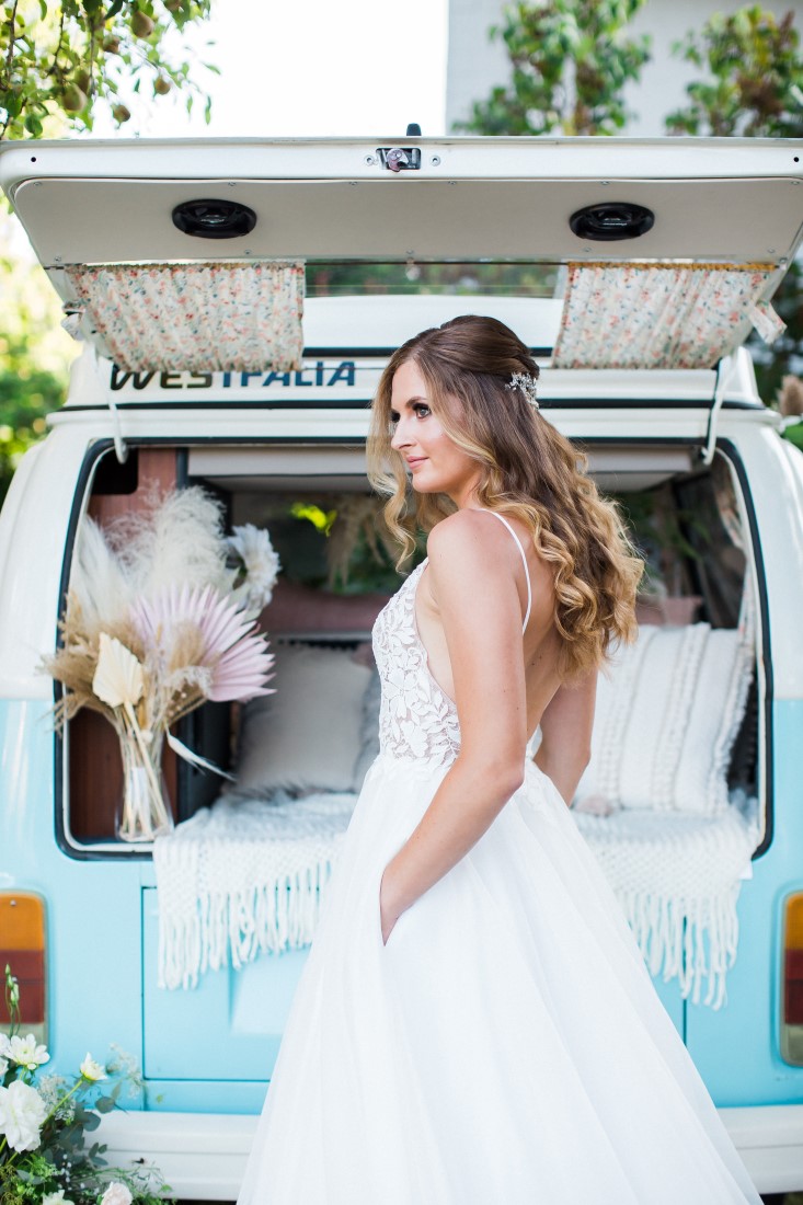 Bride with hands in the pockets of her wedding gown in front of blue and white Volkswagen Van in Vancouver