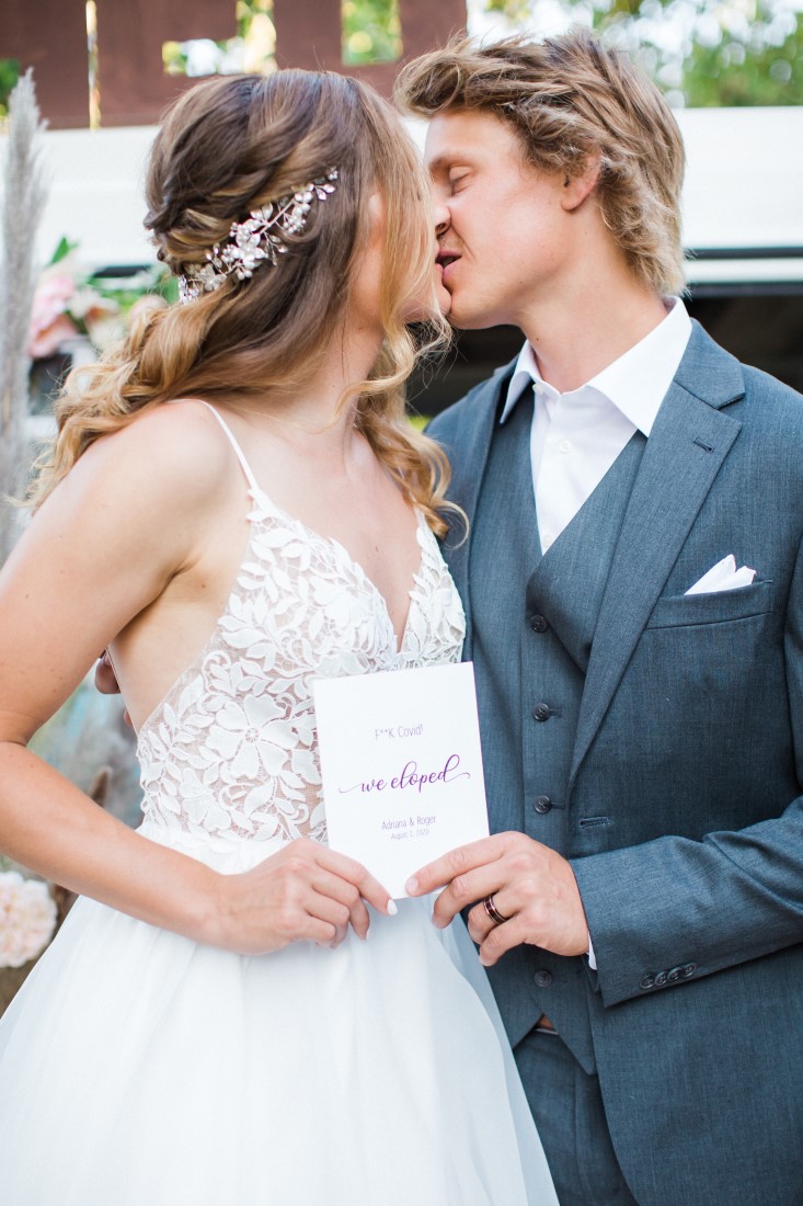 Bride and groom kiss while holding sign We Eloped Vancouver