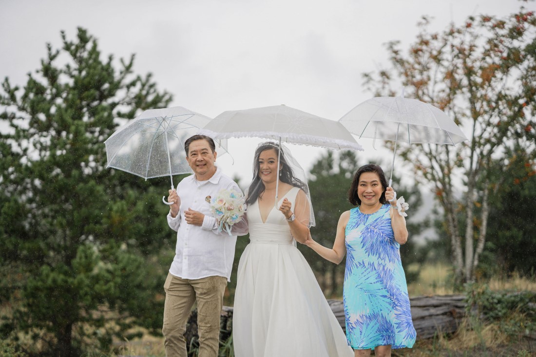 Bride walks down the aisle between her parents and holding umbrellas