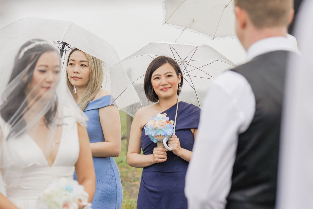 Bride arrives at beach ceremony under bridesmaids umbrellas