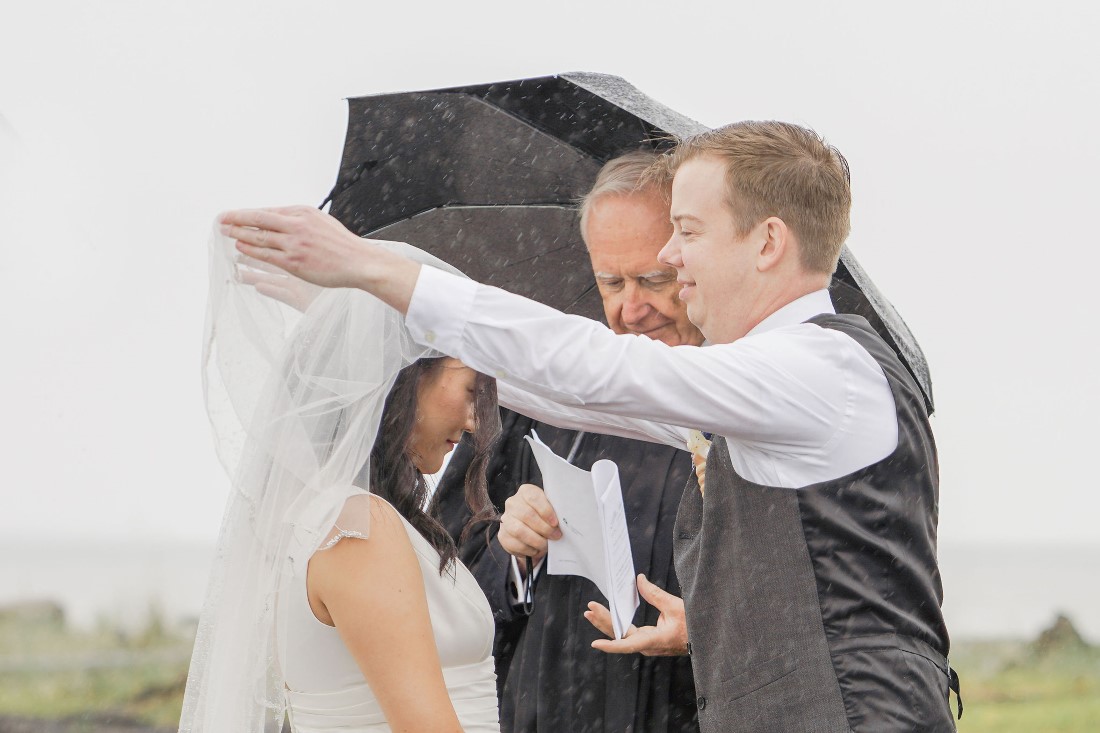 Groom pulls back bride's veil at Vancouver beach ceremony in the rain