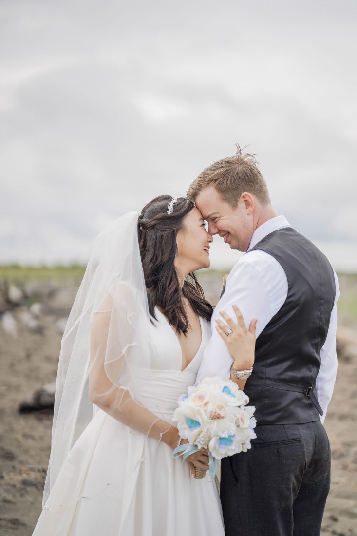 Bride carrying white floral bouquet embraces groom at Iona Beach Vancouver