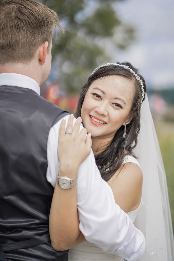 Bride smiles over her husbands shoulder at Vancouver Beach Wedding