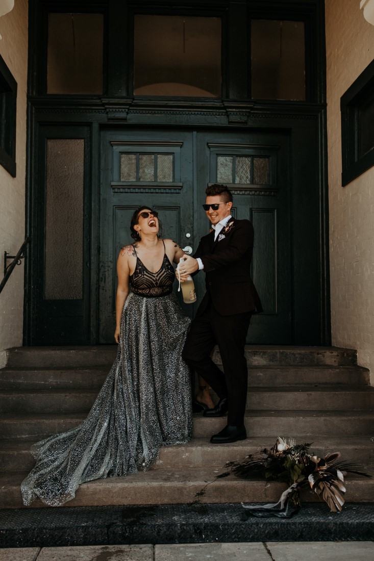 Newlyweds wearing grey and black on the steps of Powerhouse on Vancouver Island