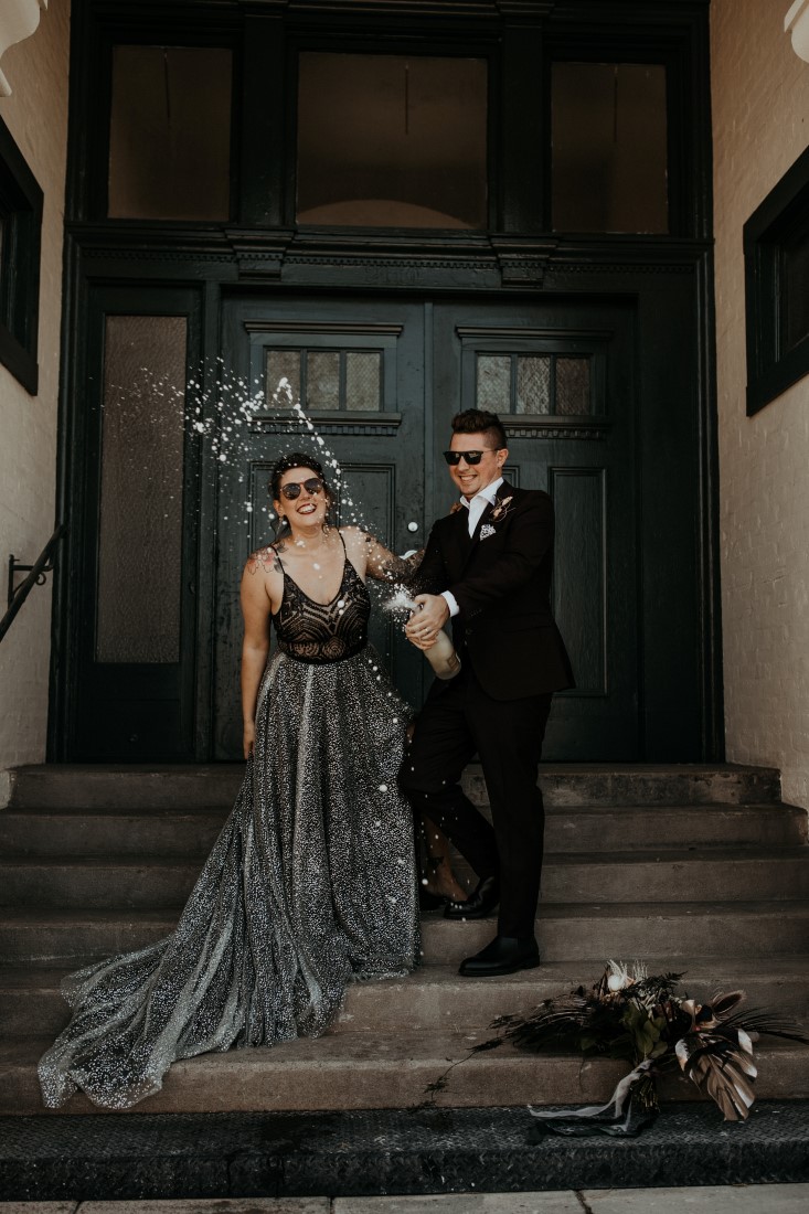 Newlyweds open bottle of champagne on the steps of Powerhouse Industrial Chic venue on Vancouver Island