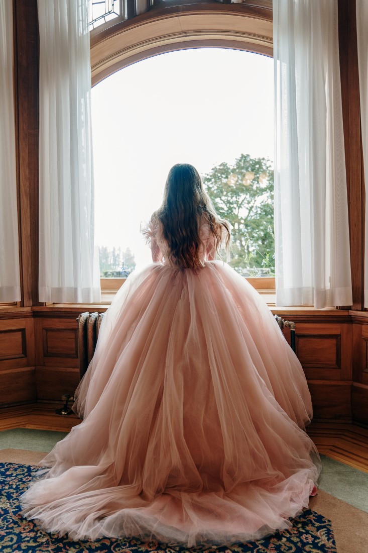 Bride looks out Hatley Castle window in her Pronovias wedding gown