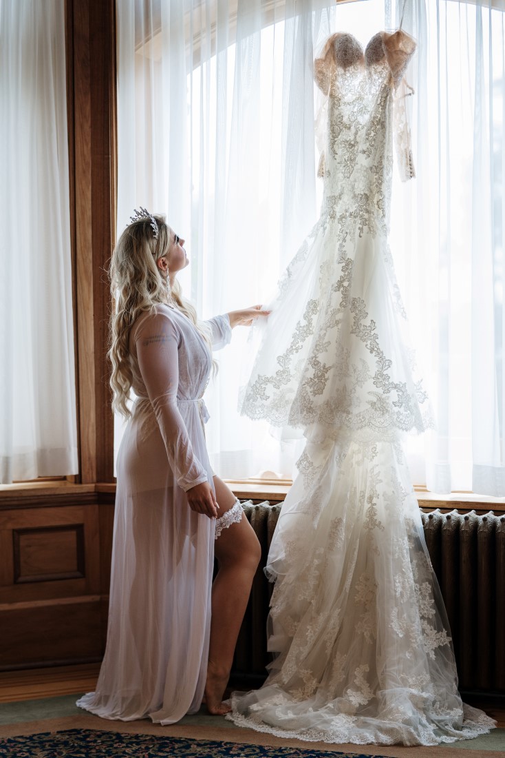 Bride touches the lace on her Pronovias wedding gown hanging in the window of Hatley Castle