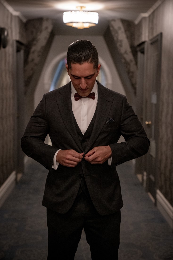 Groom buttons his tux up while standing in Hatley Castle hall on Vancouver Island