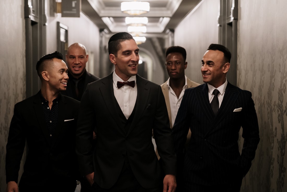 Groom and groomsmen in tuxes and bowties walk down Hatley Castle hall